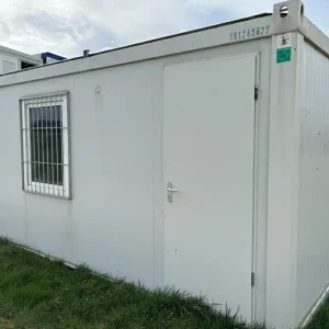 Bungalow de chantier d’occasion blanc avec porte et fenêtre sécurisée, posé sur terrain