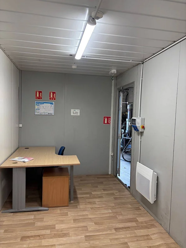 Intérieur de bungalow de chantier aménagé avec bureau, revêtement de sol et équipements de sécurité