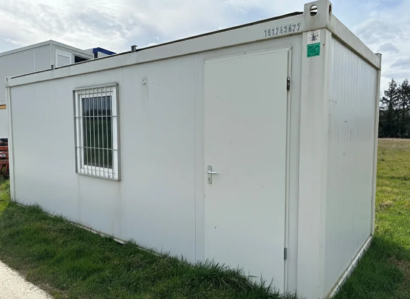 Bungalow de chantier d’occasion blanc avec porte et fenêtre sécurisée, posé sur terrain